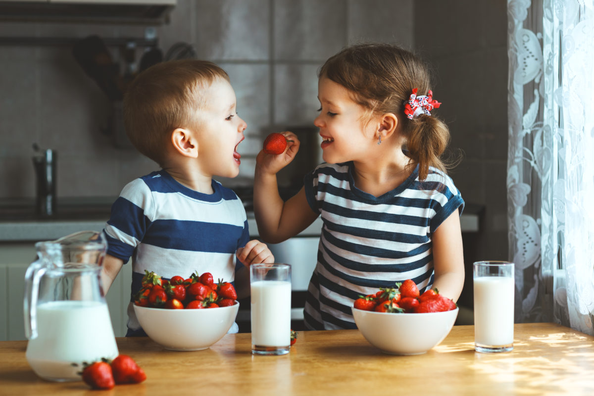 Happy children girl and boy brother and sister eating strawberries with milk